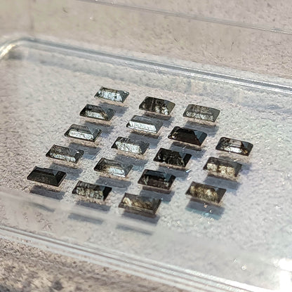 Low angled view of diamond baguettes in a clear tray, showing depth and reflections across the step-cut facets.