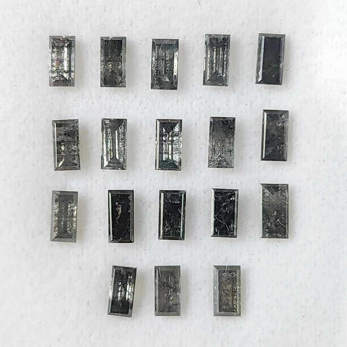 Salt and pepper diamond baguettes arranged face-up on a white display pad, showing rectangular tables, stepped edges and varied inclusions.