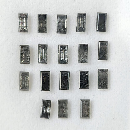 Salt and pepper diamond baguettes arranged face-up on a white display pad, showing rectangular tables, stepped edges and varied inclusions.