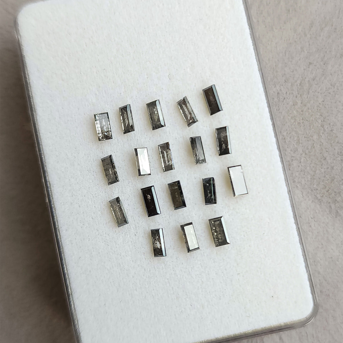Tilted white display pad with rows of diamond baguettes, showing changing reflections across their rectangular step cuts.