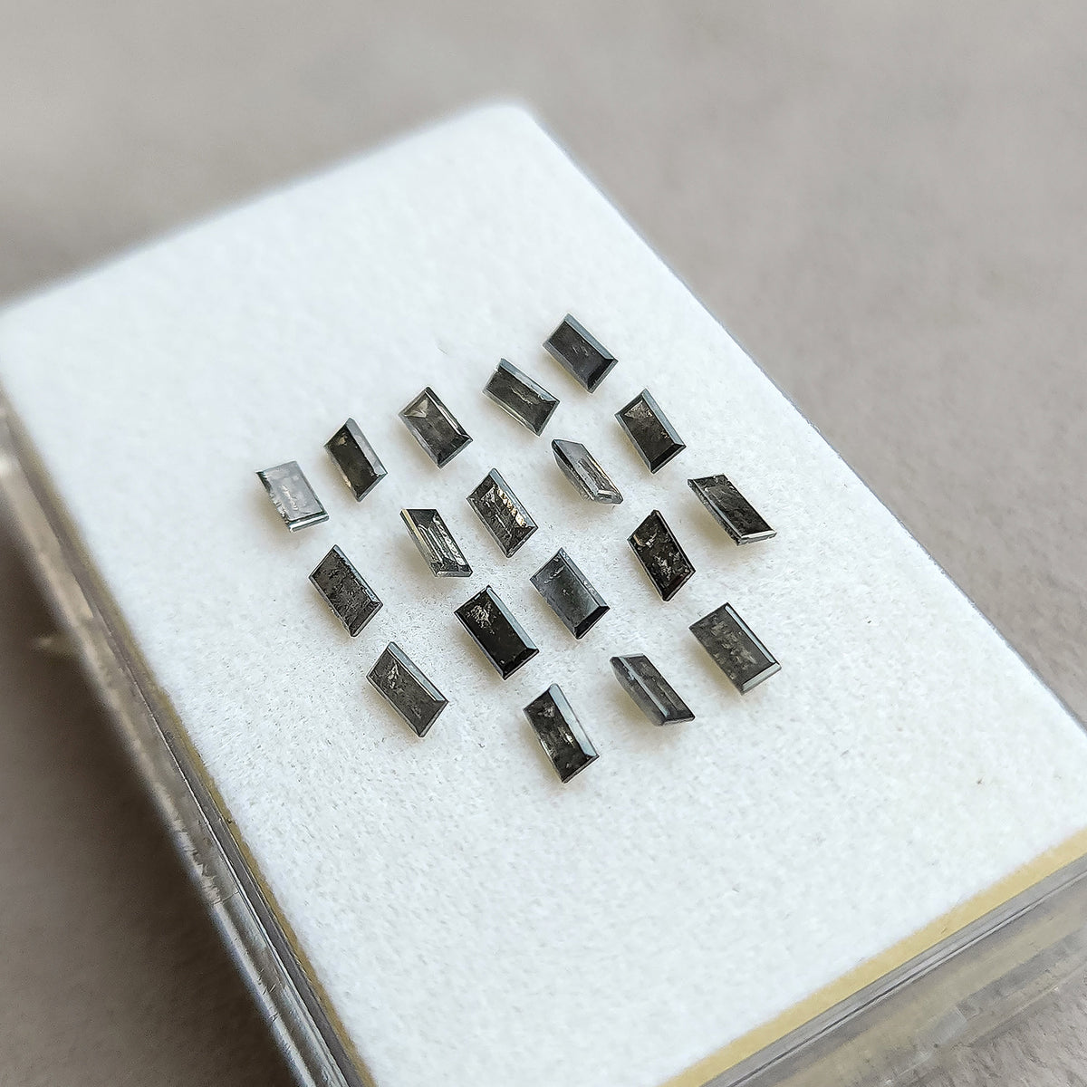 Oblique view of salt and pepper diamond baguettes on a white display pad, with the case outline visible.