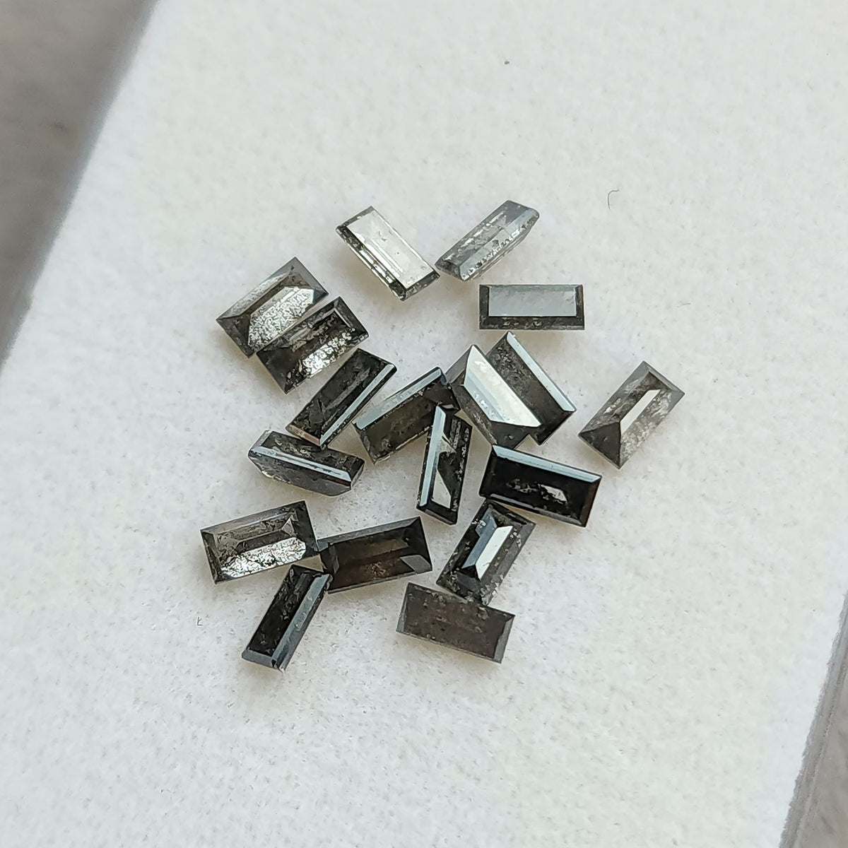 Salt and pepper diamond baguettes scattered on a white display pad, showing individual facets and inclusion patterns.