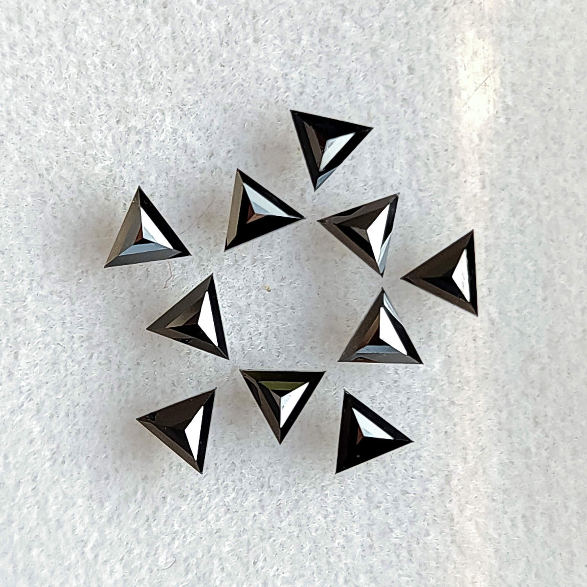 Group of black triangular diamonds on white fabric, displaying centrally converging facets from the opposite side.