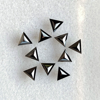 Group of black triangular diamonds on white fabric, displaying centrally converging facets from the opposite side.