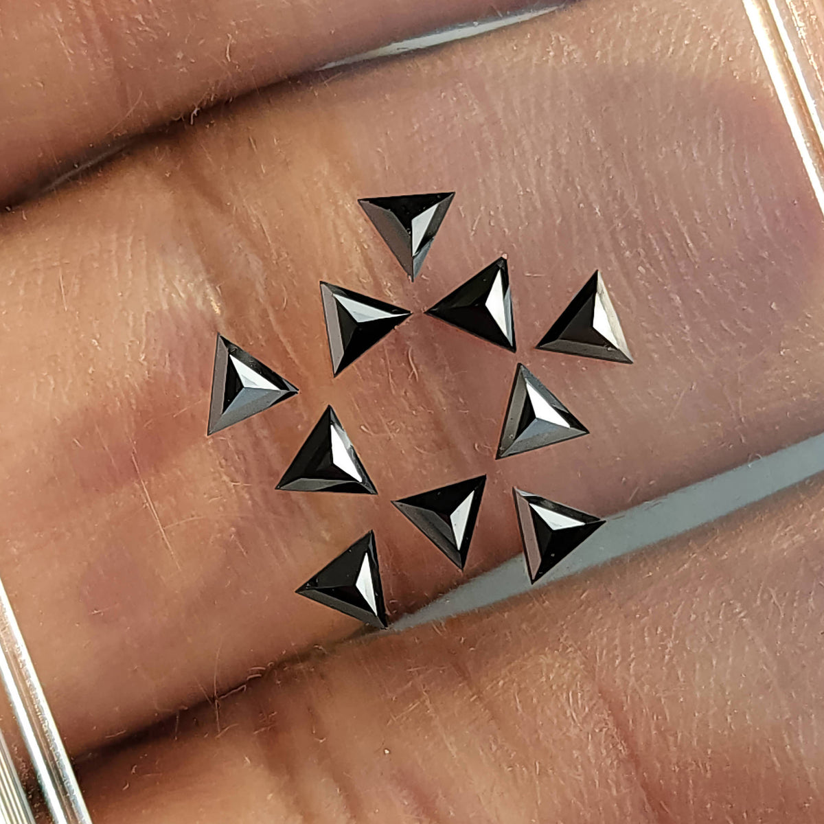 Black triangular diamonds resting on a finger, with raised angular facets and bright edge reflections.