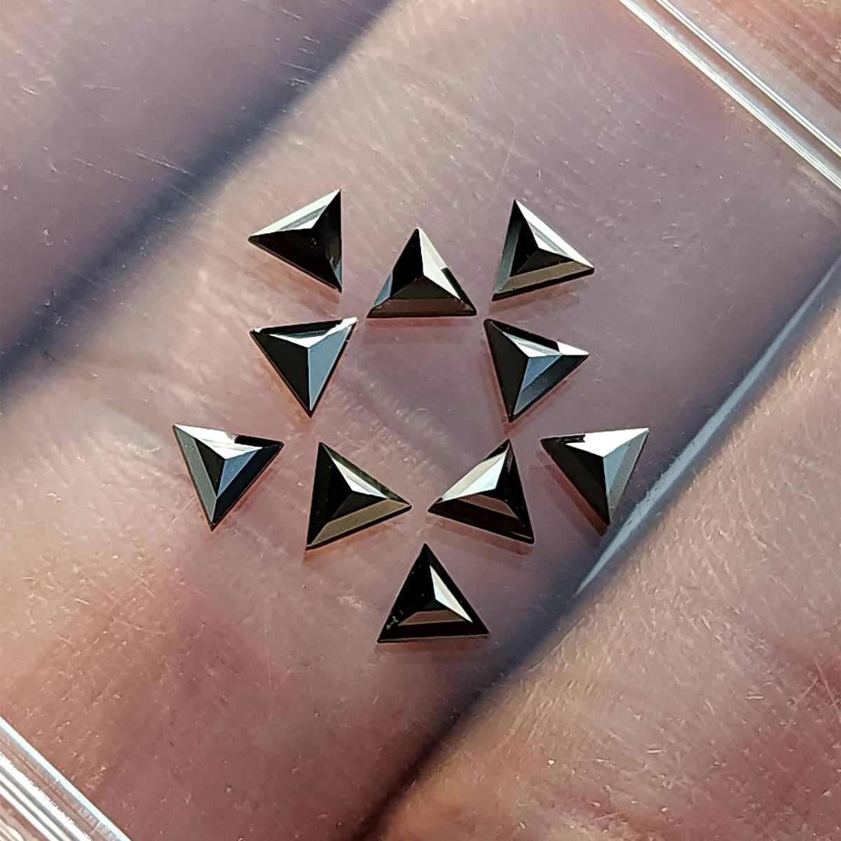 Black triangular diamonds arranged on a clear tray over skin, showing alternating black and silvery facets.