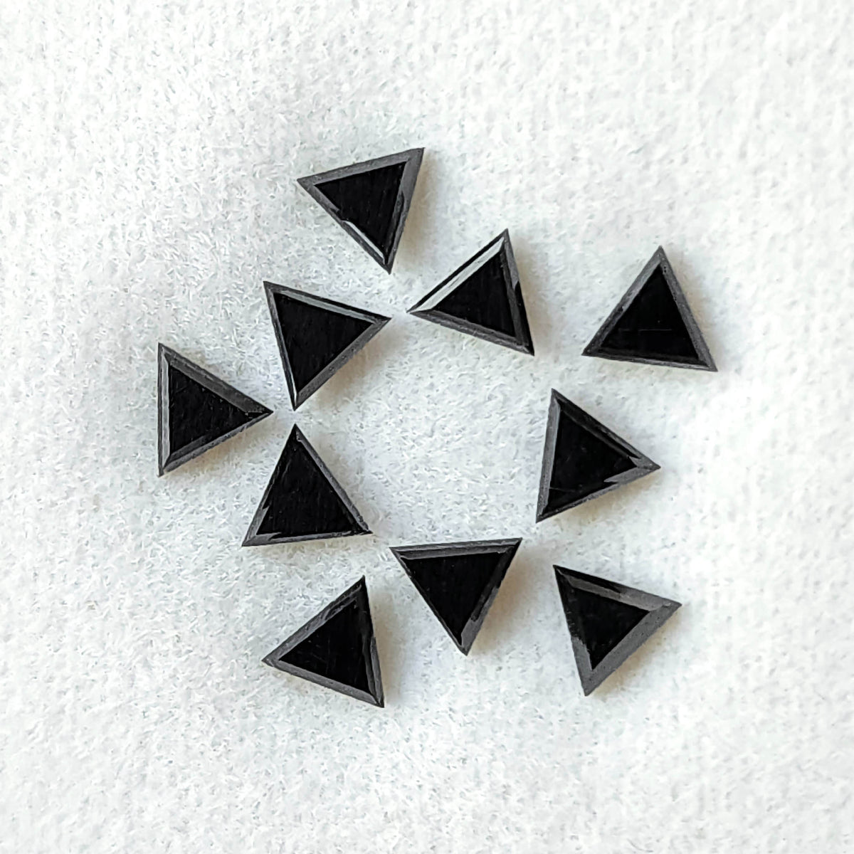 Black triangular diamonds grouped on a pale pad, with dark flat tables bounded by fine reflective edges.