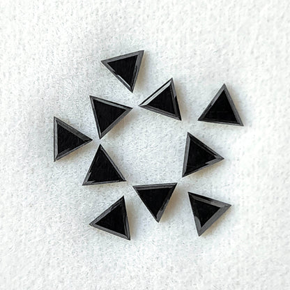 Black triangular diamonds grouped on a pale pad, with dark flat tables bounded by fine reflective edges.