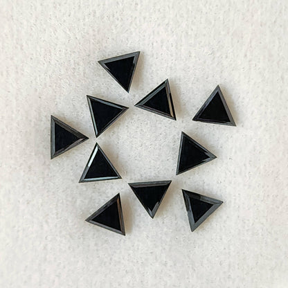 Ten black triangular diamonds on a white textured pad, showing broad flat triangular tables and narrow surrounding facets.