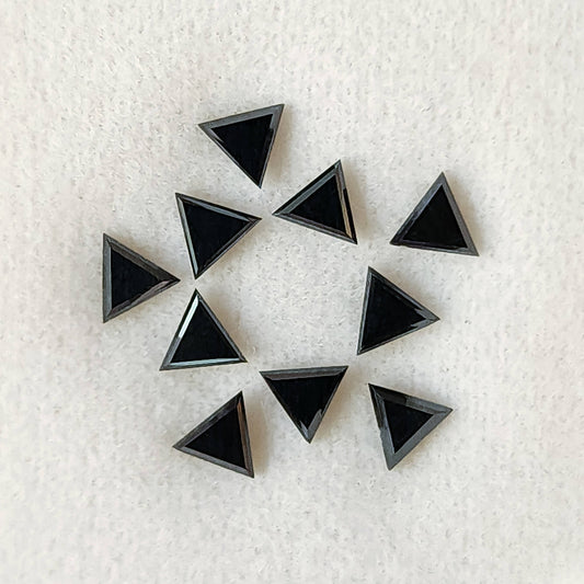 Ten black triangular diamonds on a white textured pad, showing broad flat triangular tables and narrow surrounding facets.