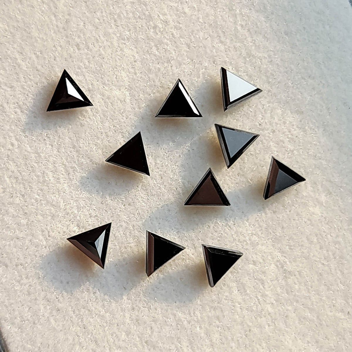 Black triangular diamonds at varied angles on a pale pad, showing dark faces and bright reflected facets.