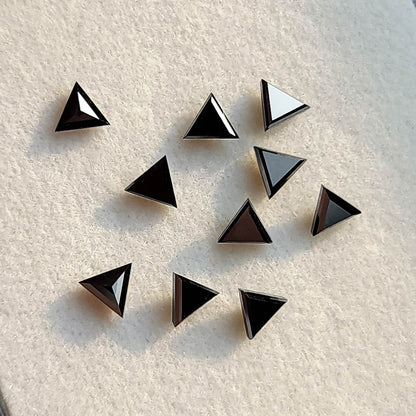 Black triangular diamonds at varied angles on a pale pad, showing dark faces and bright reflected facets.