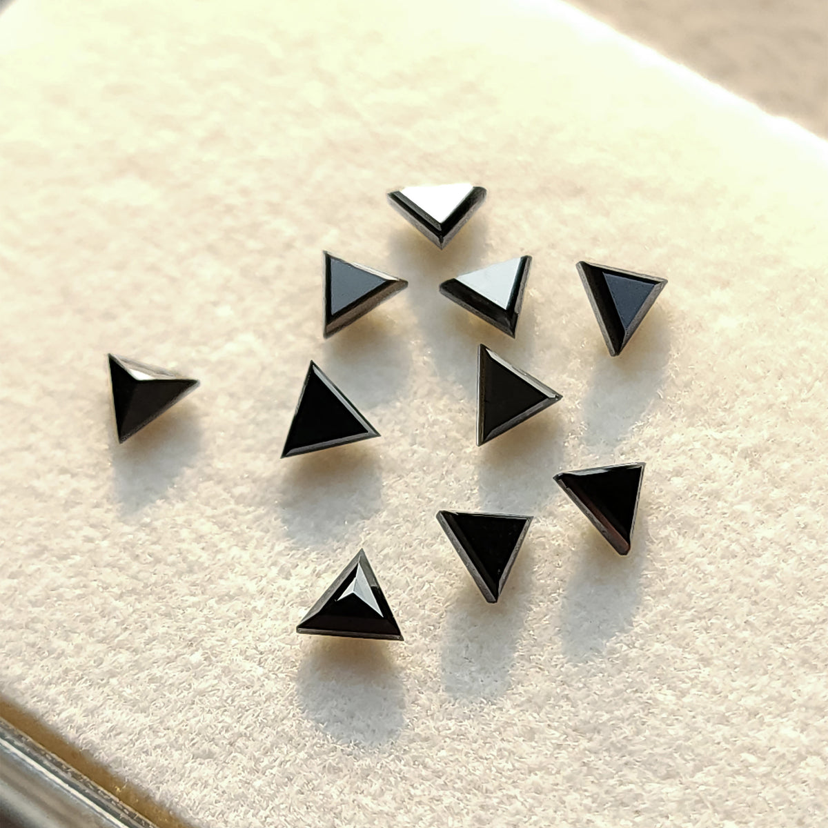 Black triangular diamonds on a white tray in bright light, showing dark tables and reflective edges.