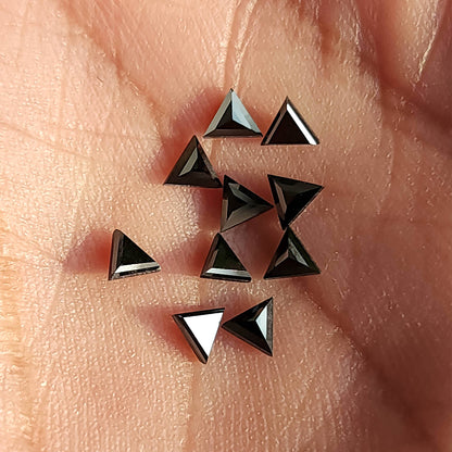 Loose black triangular diamonds on a palm, showing different facet reflections and relative scale.