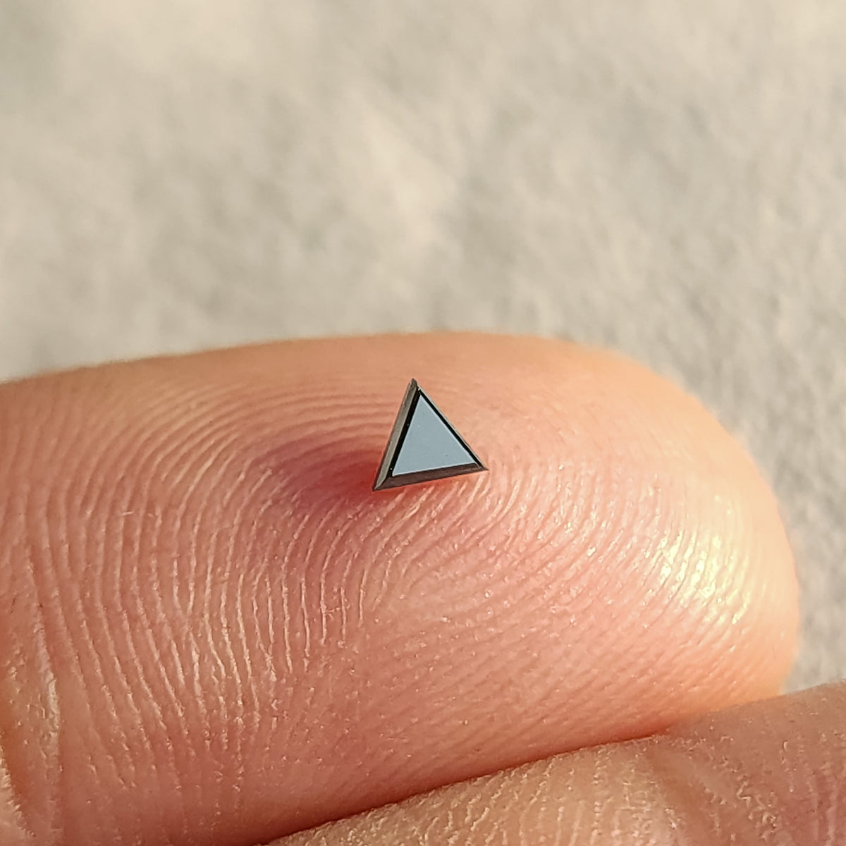 One triangular black diamond on a fingertip, with a bright reflection across the flat table, for relative scale.