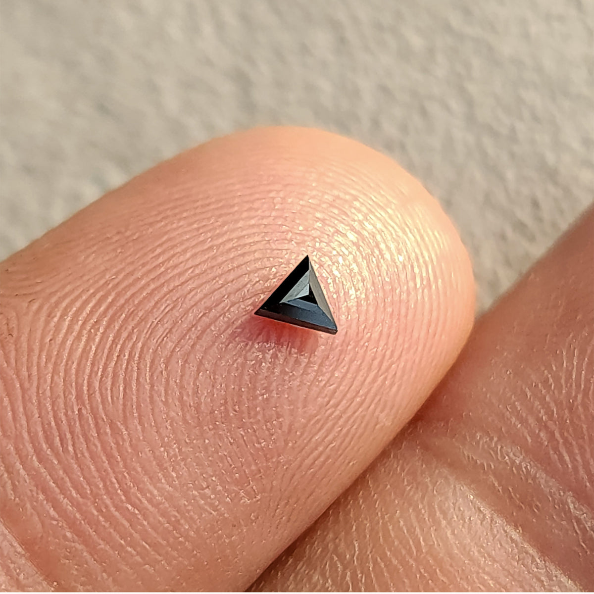 One black triangular diamond on a fingertip, with the opposite-side facets meeting near the center.