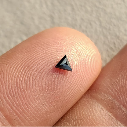 One black triangular diamond on a fingertip, with the opposite-side facets meeting near the center.
