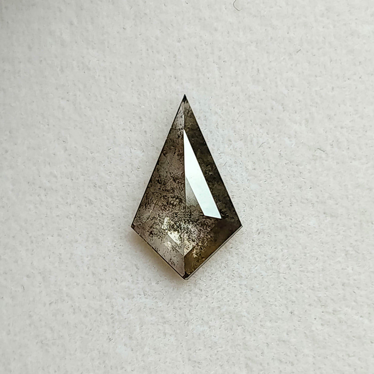 Face-up view of a kite shaped salt and pepper lab-grown diamond with dark grey inclusions, resting on a textured white background.