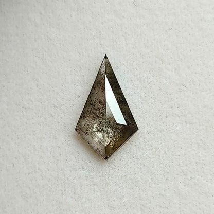 Face-up view of a kite shaped salt and pepper lab-grown diamond with dark grey inclusions, resting on a textured white background.