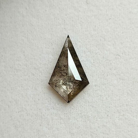 Face-up view of a kite shaped salt and pepper lab-grown diamond with dark grey inclusions, resting on a textured white background.