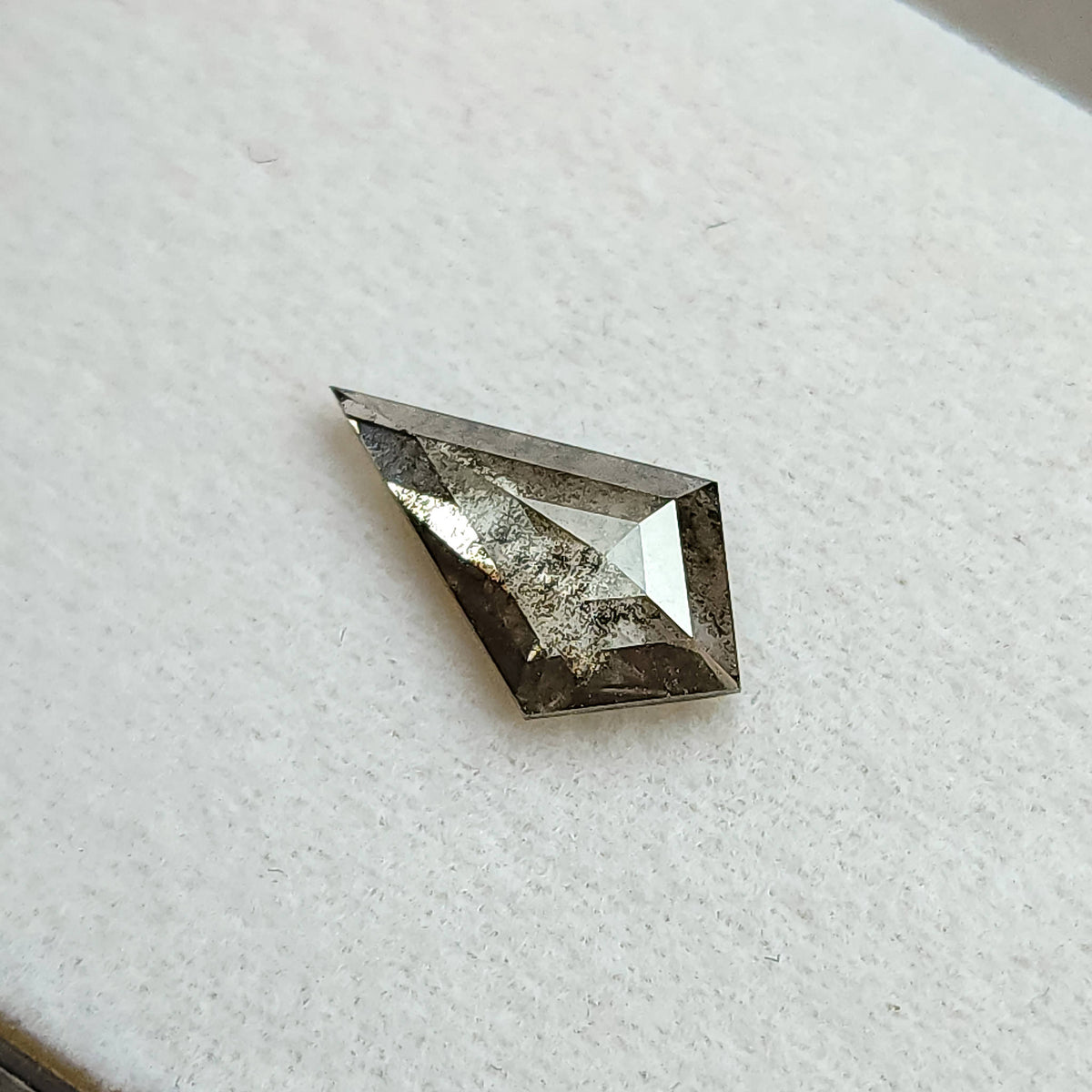 Face-up view of a gray, kite-shaped salt and pepper lab-grown diamond resting on a white textured background.