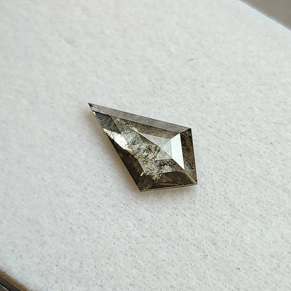 Face-up view of a gray, kite-shaped salt and pepper lab-grown diamond resting on a white textured background.