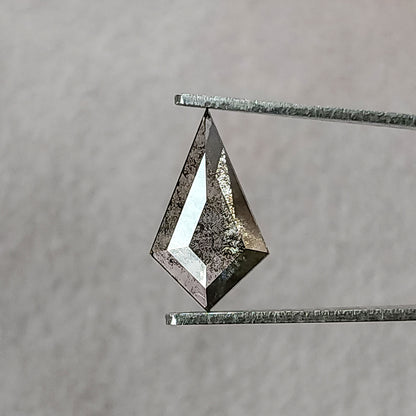 Face-up view of a kite-shaped salt and pepper lab-grown diamond held in metal tweezers against a light grey background.