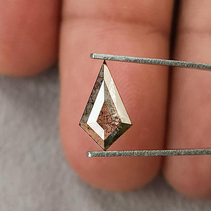 Face-up view of a grey kite-shaped salt and pepper lab-grown diamond held in tweezers against a blurred background of fingers.