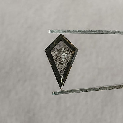 Face-up view of a kite-shaped salt and pepper lab-grown diamond held in tweezers against a plain light grey background.