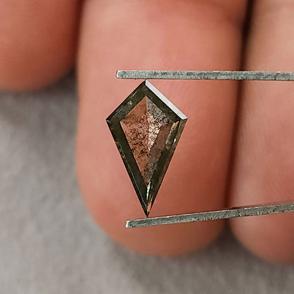 Face-up view of a kite-shaped salt and pepper lab-grown diamond with greyish-brown tones, held in tweezers against blurred fingers.