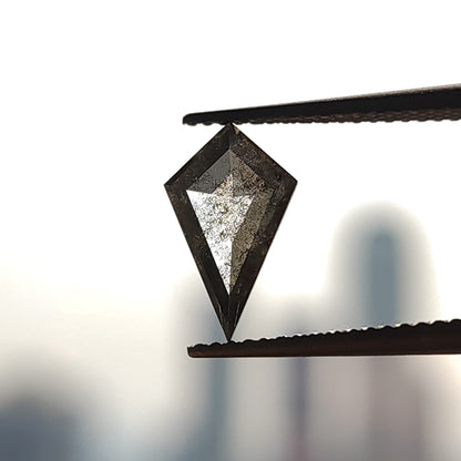 Face-up view of a kite-shaped salt and pepper lab-grown diamond held vertically in tweezers against a blurred background.