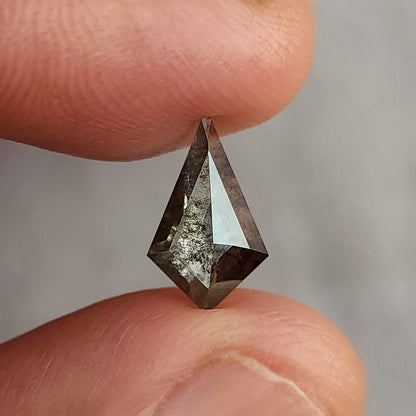 Face-up view of a kite-shaped dark grey salt and pepper lab-grown diamond held between two fingertips over a plain light background.