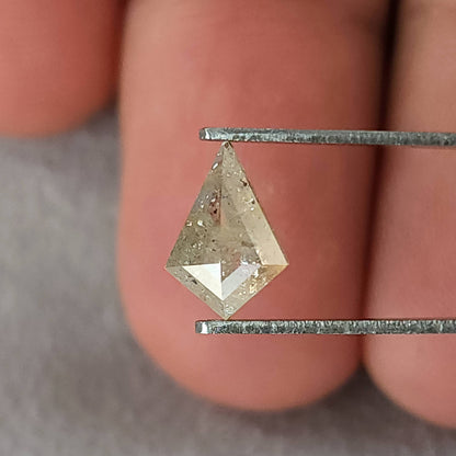 The kite-shaped natural diamond held in tweezers near fingers for scale, with pale champagne-gray reflections.