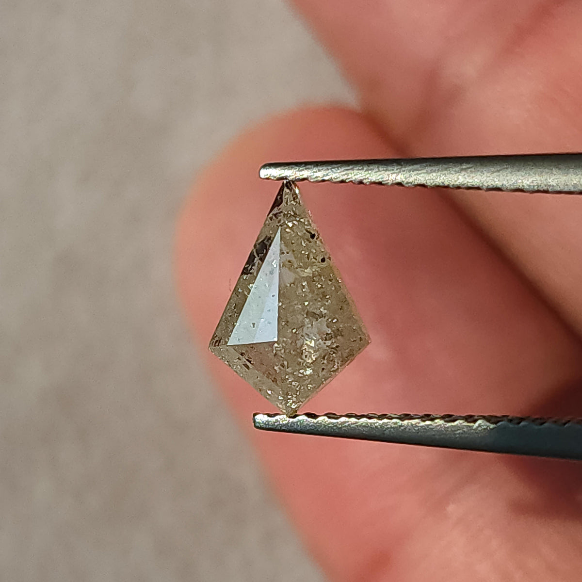 Angled view of the untreated kite diamond in tweezers, showing the pointed outline and reflective rose-cut facets.
