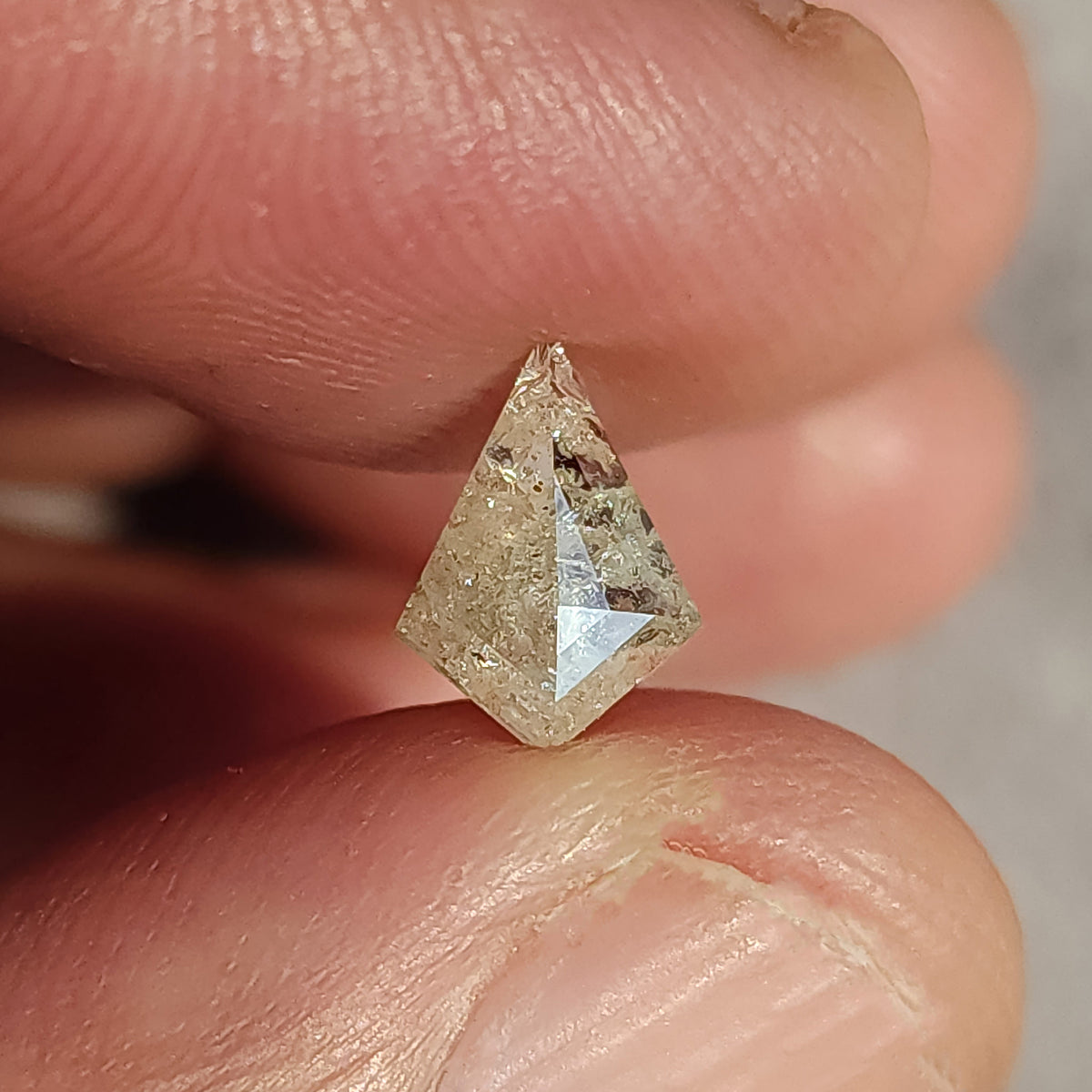 The 0.92 ct kite diamond held between fingers for scale, showing its elongated geometric outline.