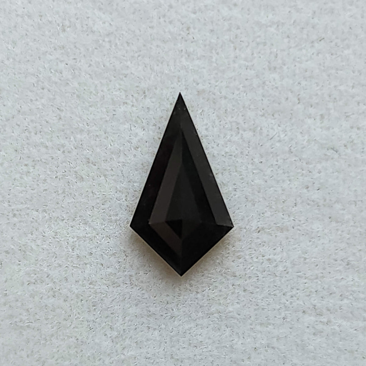 Vista superior de un diamante negro sólido, talla cometa geométrica, sobre fondo blanco texturizado.