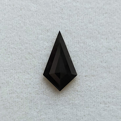 Vista superior de un diamante negro sólido, talla cometa geométrica, sobre fondo blanco texturizado.