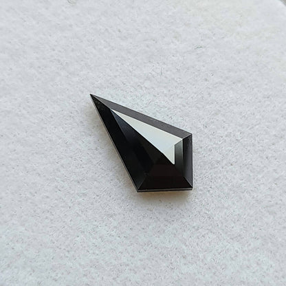 Vista inclinada de un diamante negro, talla cometa geométrica, sobre fondo blanco, resaltando un reflejo brillante en una faceta.
