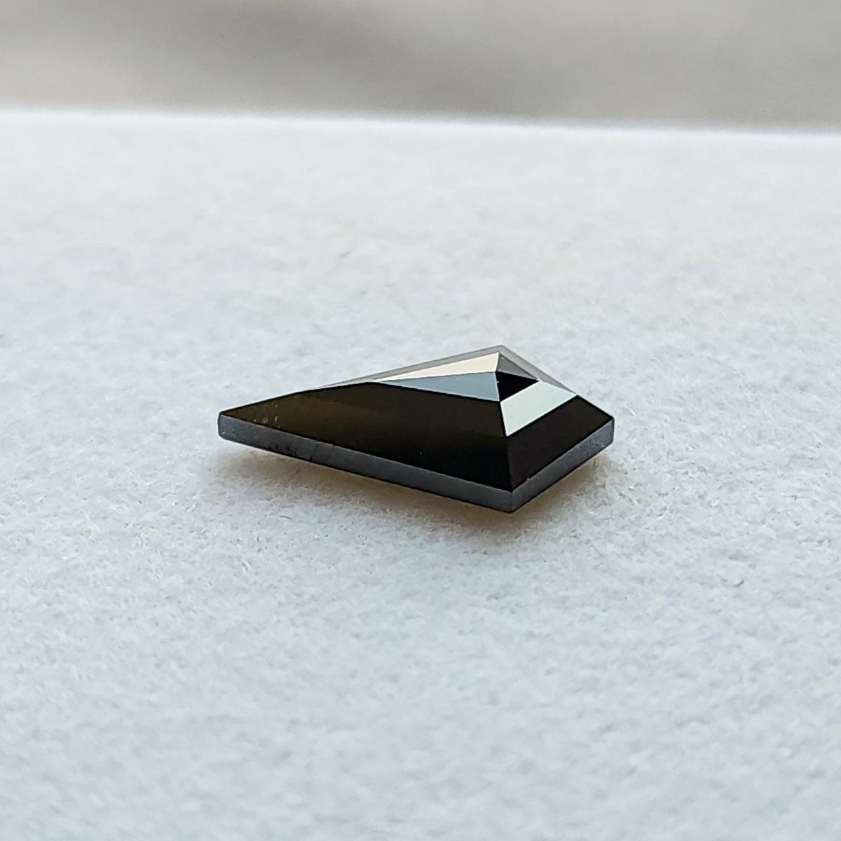 Ángulo de perfil bajo de un diamante negro talla cometa geométrica sobre fondo blanco, mostrando la profundidad de la piedra.