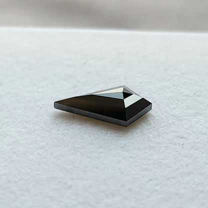 Ángulo de perfil bajo de un diamante negro talla cometa geométrica sobre fondo blanco, mostrando la profundidad de la piedra.