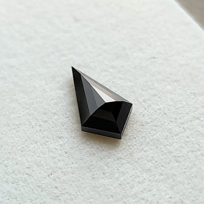Ángulo inclinado en primer plano de un diamante negro talla cometa geométrica sobre una superficie blanca texturizada.