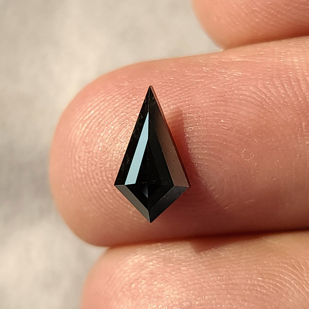 Vista frontal de un diamante negro, talla cometa geométrica, descansando sobre dos dedos.