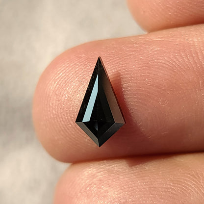 Vista frontal de un diamante negro, talla cometa geométrica, descansando sobre dos dedos.
