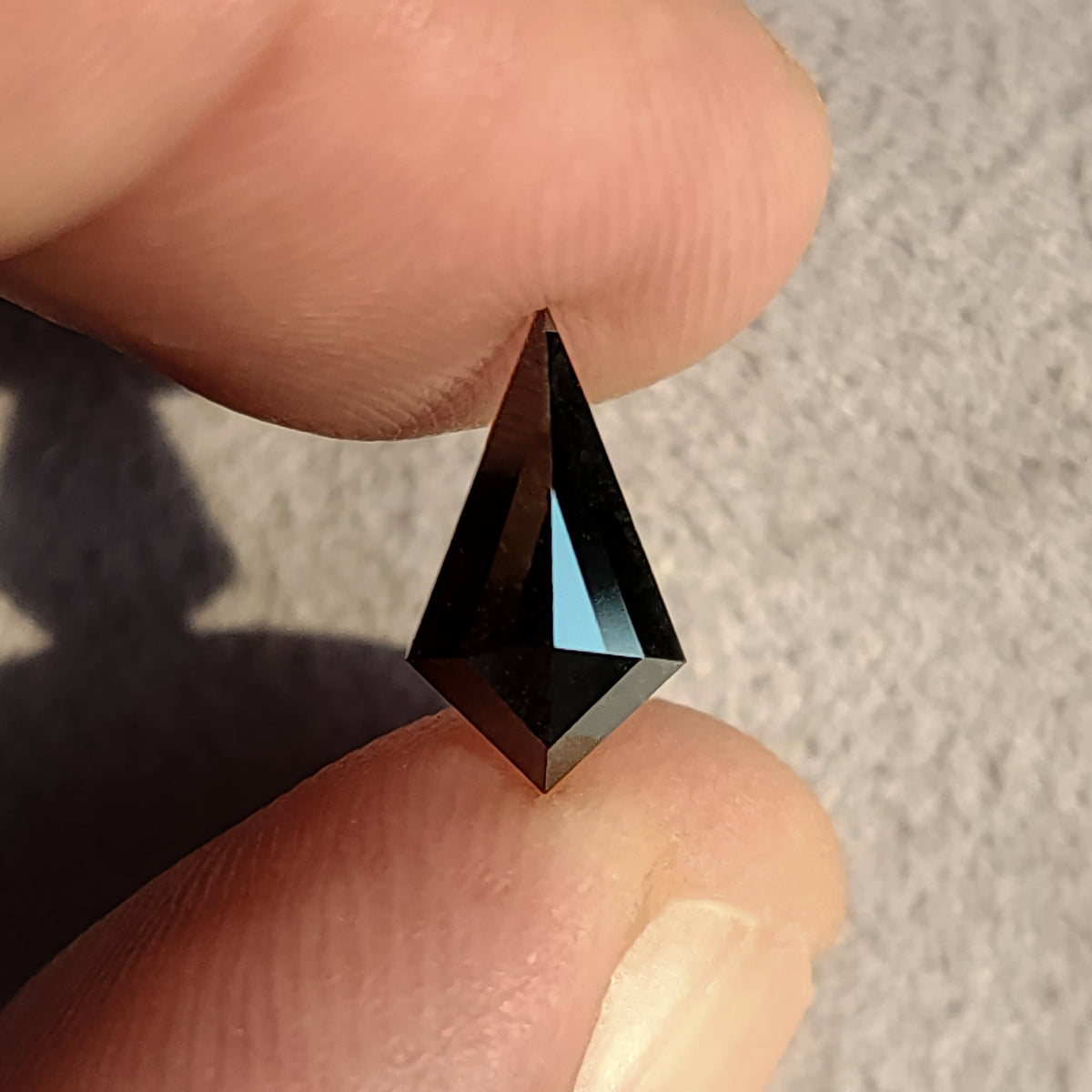 Diamante negro, talla cometa geométrica, sostenido entre el pulgar y el índice, mostrando un reflejo brillante en la faceta de la tabla.