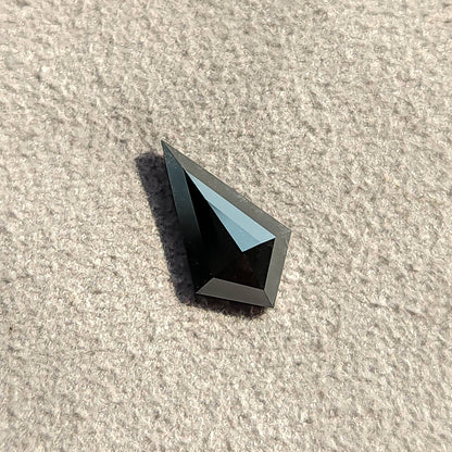Vista inclinada de un diamante negro talla cometa bajo luz intensa, proyectando una sombra oscura sobre un fondo blanco.