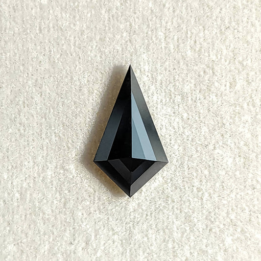 Face-up view of a black geometric kite cut diamond resting on a white textured background.