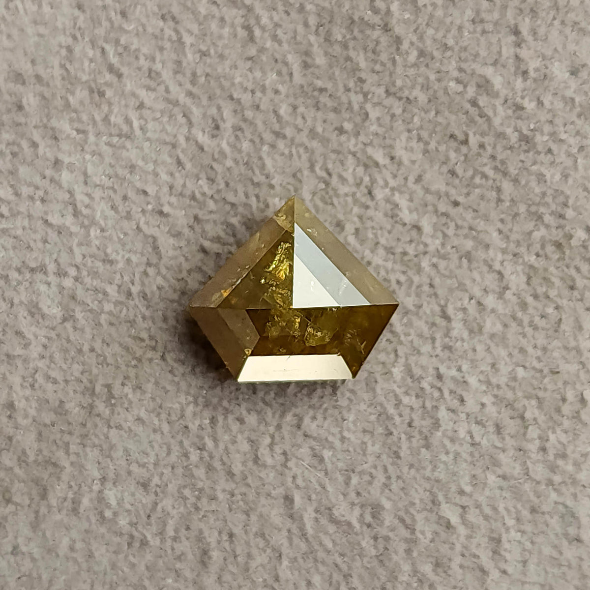 Face-up view of the warm yellow-brown shield diamond in tweezers, showing its pointed outline and reflective facets.