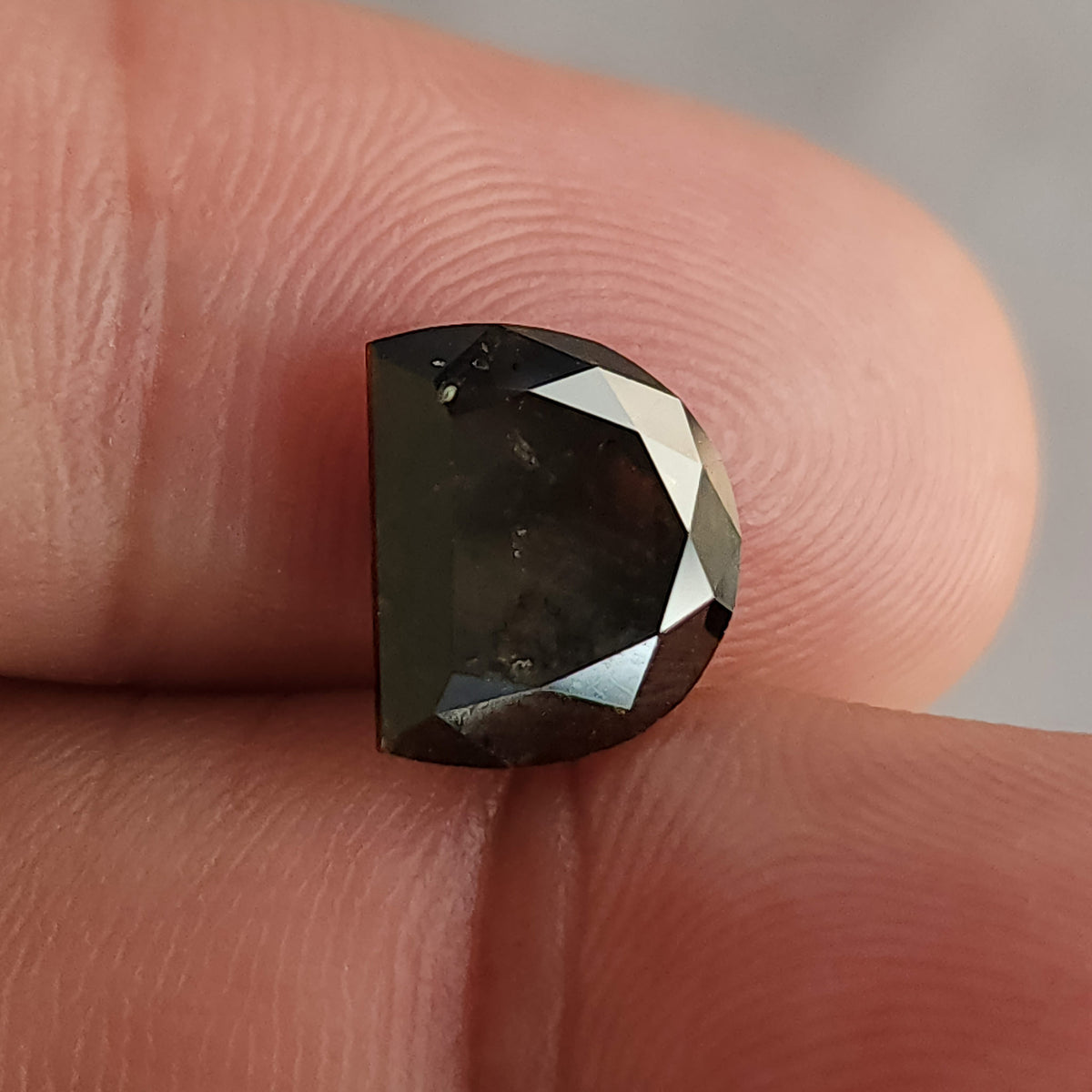 Close-up of a dark brown D-shaped gemstone resting on fingers, revealing subtle surface characteristics across its large flat facet.