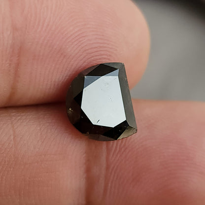 D-shaped dark gemstone lying flat on a finger, with a large, bright central facet reflection and dark surrounding step-like edges.