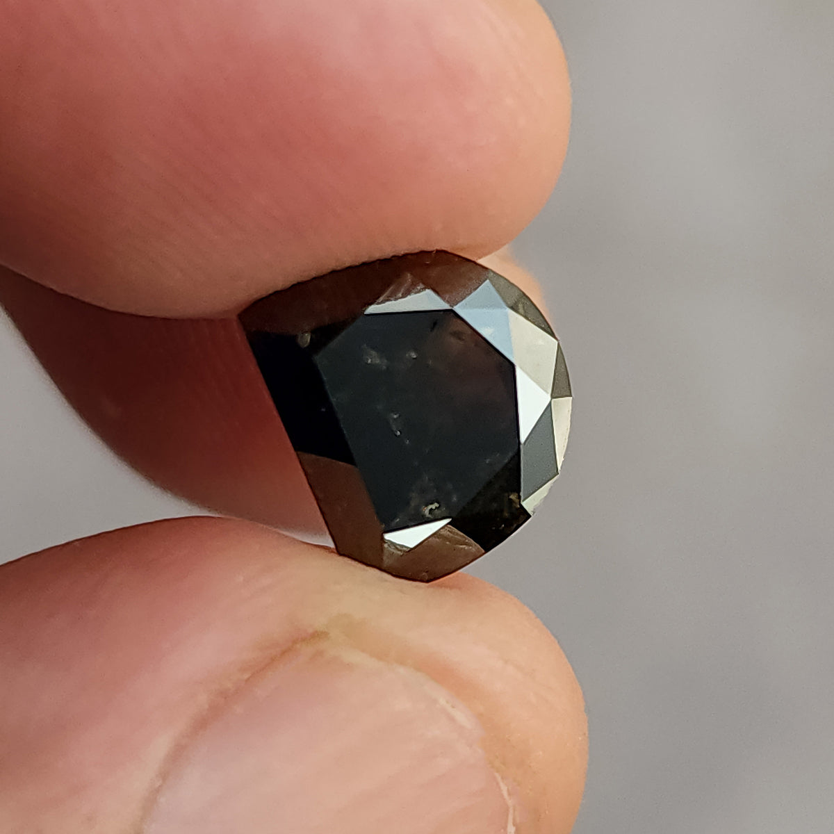 Close-up of a dark brown half-moon shaped gemstone held by fingers, showing deep internal color and small visible surface details.
